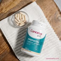 Conceive Plus prenatal supplement bottle with capsules on a wooden surface